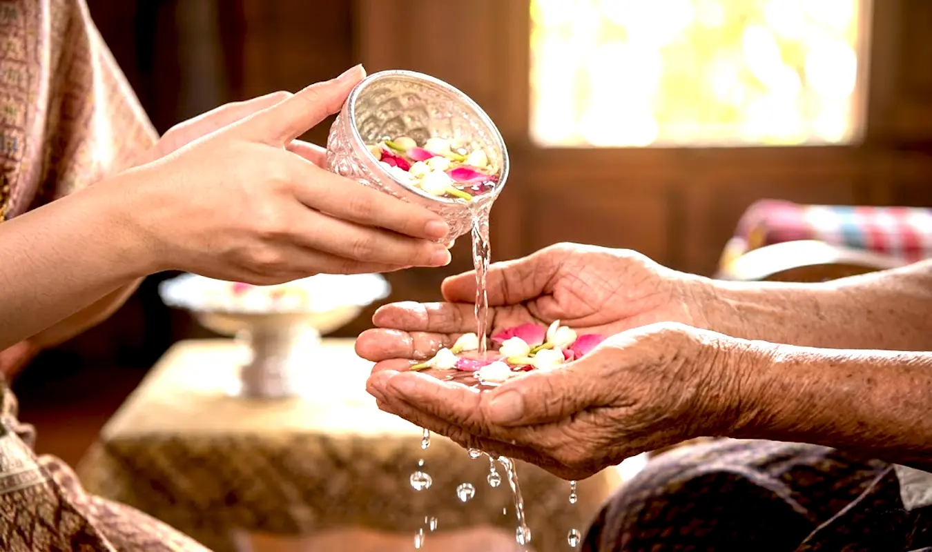Traditional Thai Rod Nam Dam Hua ceremony during Songkran, pouring scented jasmine water on elderly hands as a gesture of gratitude and respect.