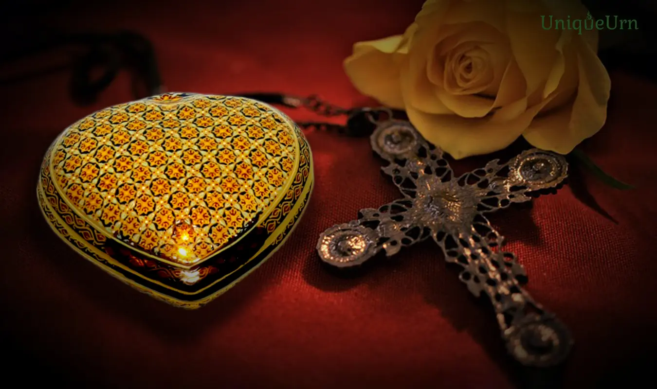Handcrafted Bencharong heart keepsake urn from UniqueUrn sits beside the cross and yellow rose.