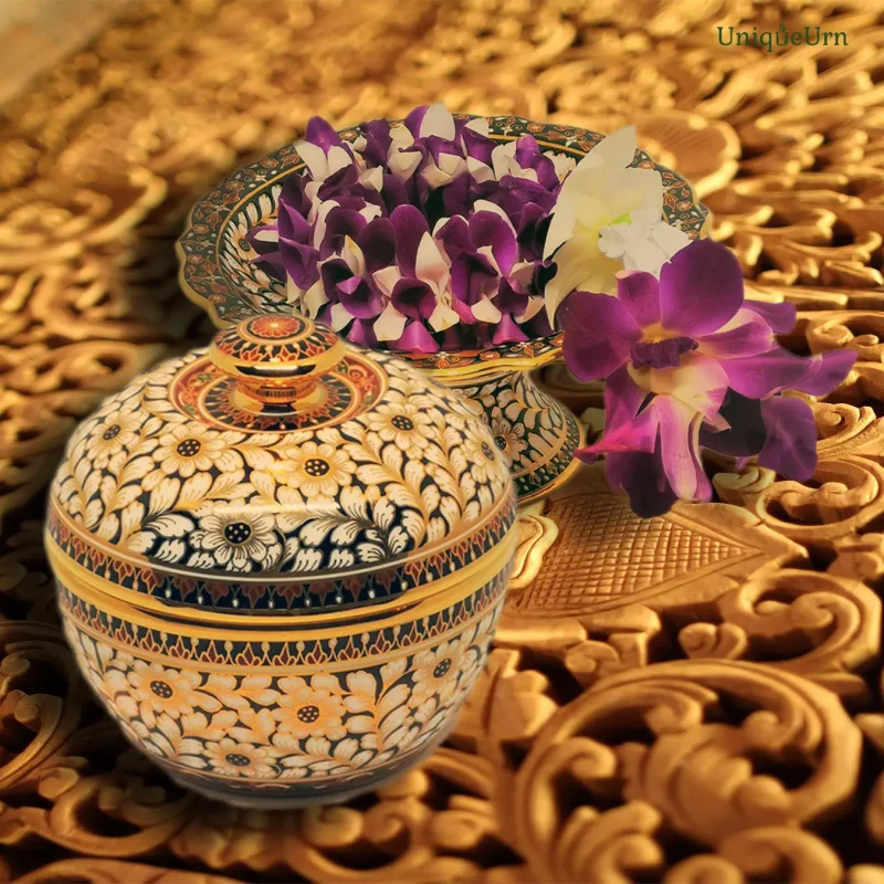 Picture of a hand-painted Bencharong art keepsake urn for ashes and stem plate by UniqueUrn at the level with an orchid garland that represents respect. All placed on a beautifully carved teak table.
