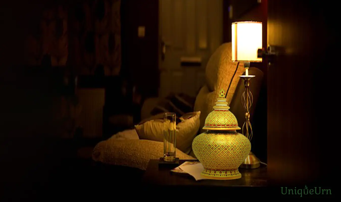 A master artisan's hand-painted geometry Pikul yellow design, hand-painted on a porcelain Bencharong Thomayomjukchad cremation urn, sits on a sofa side table next to the lamp.